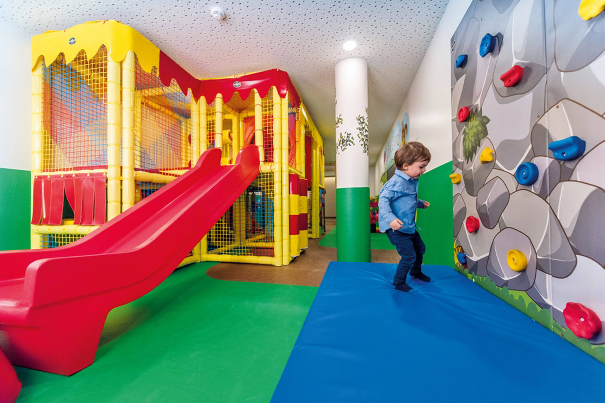 Ein kleines Kind, das in einem Indoor-Spielplatz an einer Kletterwand spielt. - Hotel DAS ROYAL