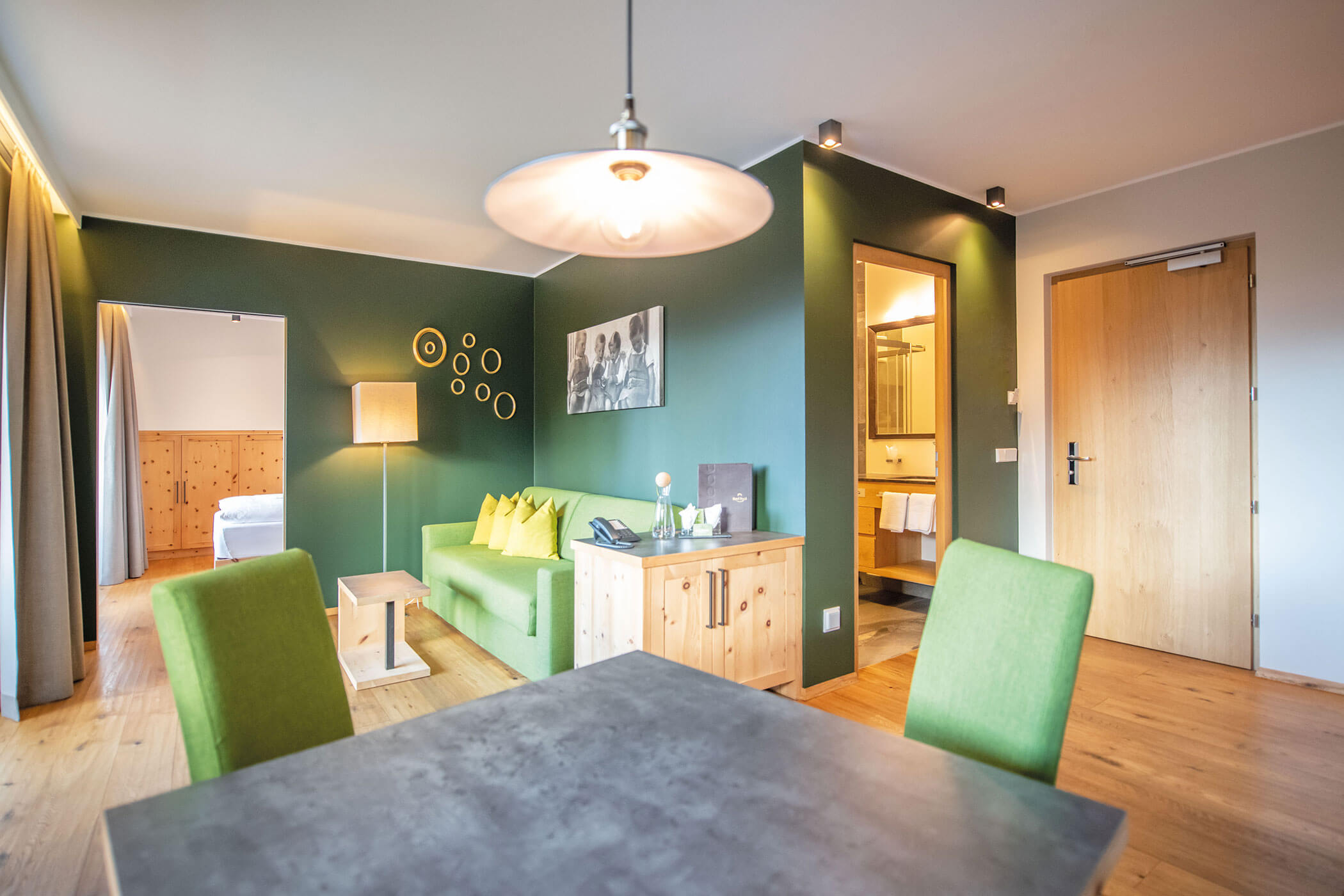 Hotelzimmer mit einem grünen Sofa, einem Holzschrank und einer Essecke. - Hotel DAS ROYAL