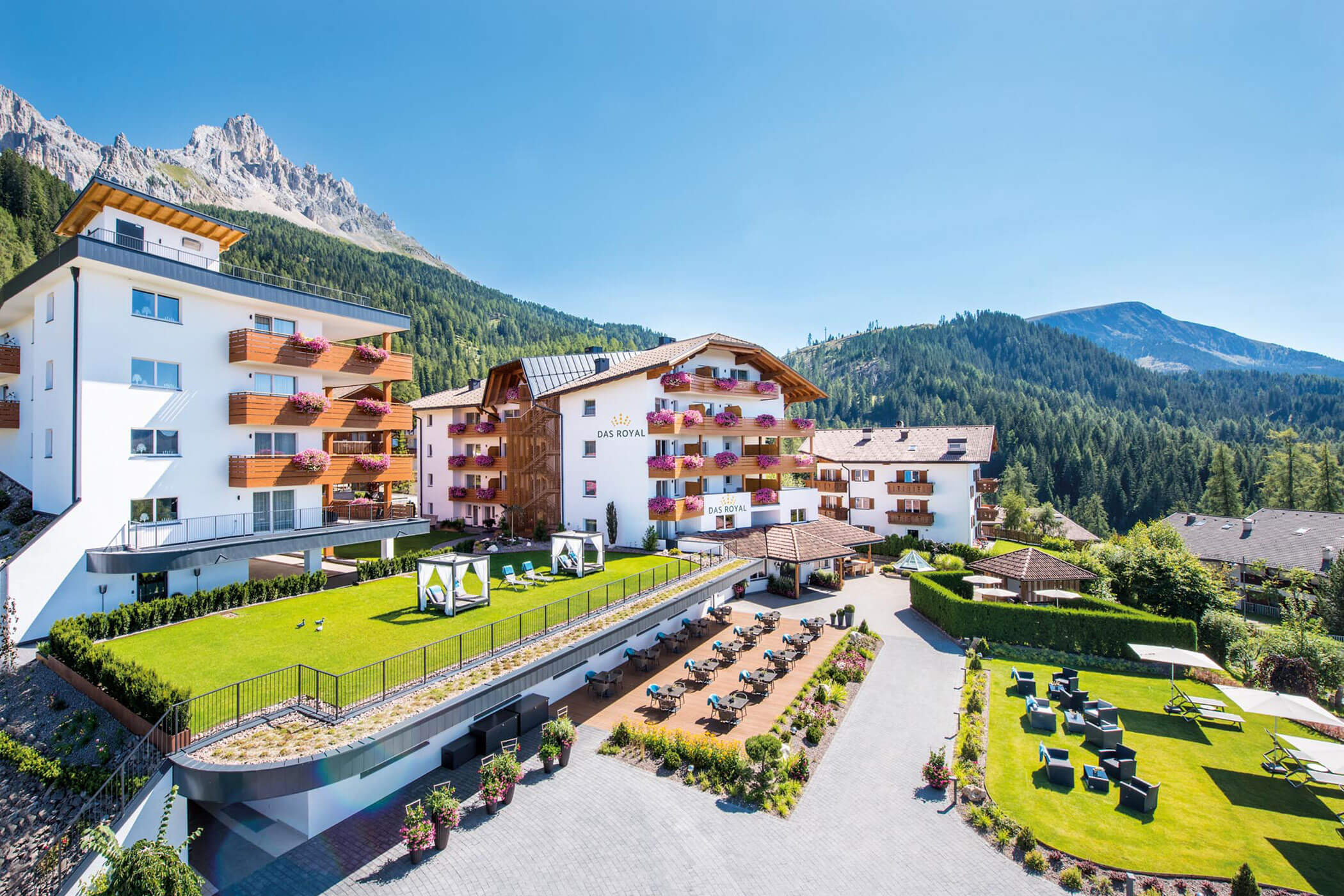 Das Royal Hotel Resort mit Balkonen, Rasenflächen und Sitzgelegenheiten im Freien vor der Kulisse der Berggipfel. - Hotel DAS ROYAL