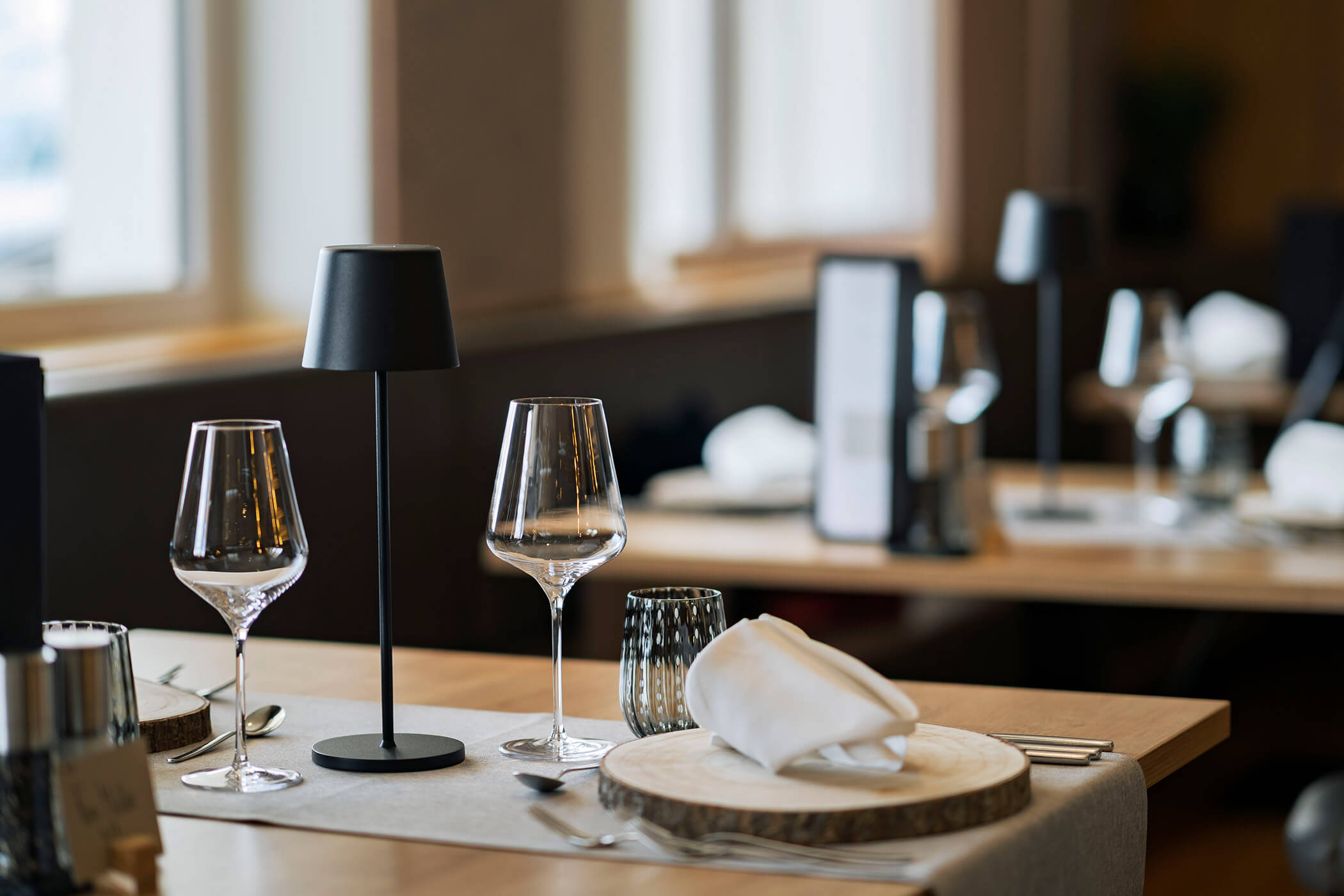 Ein gedeckter Tisch in einem Restaurant mit Weingläsern, einer kleinen Lampe und einer gefalteten Serviette. - Hotel DAS ROYAL