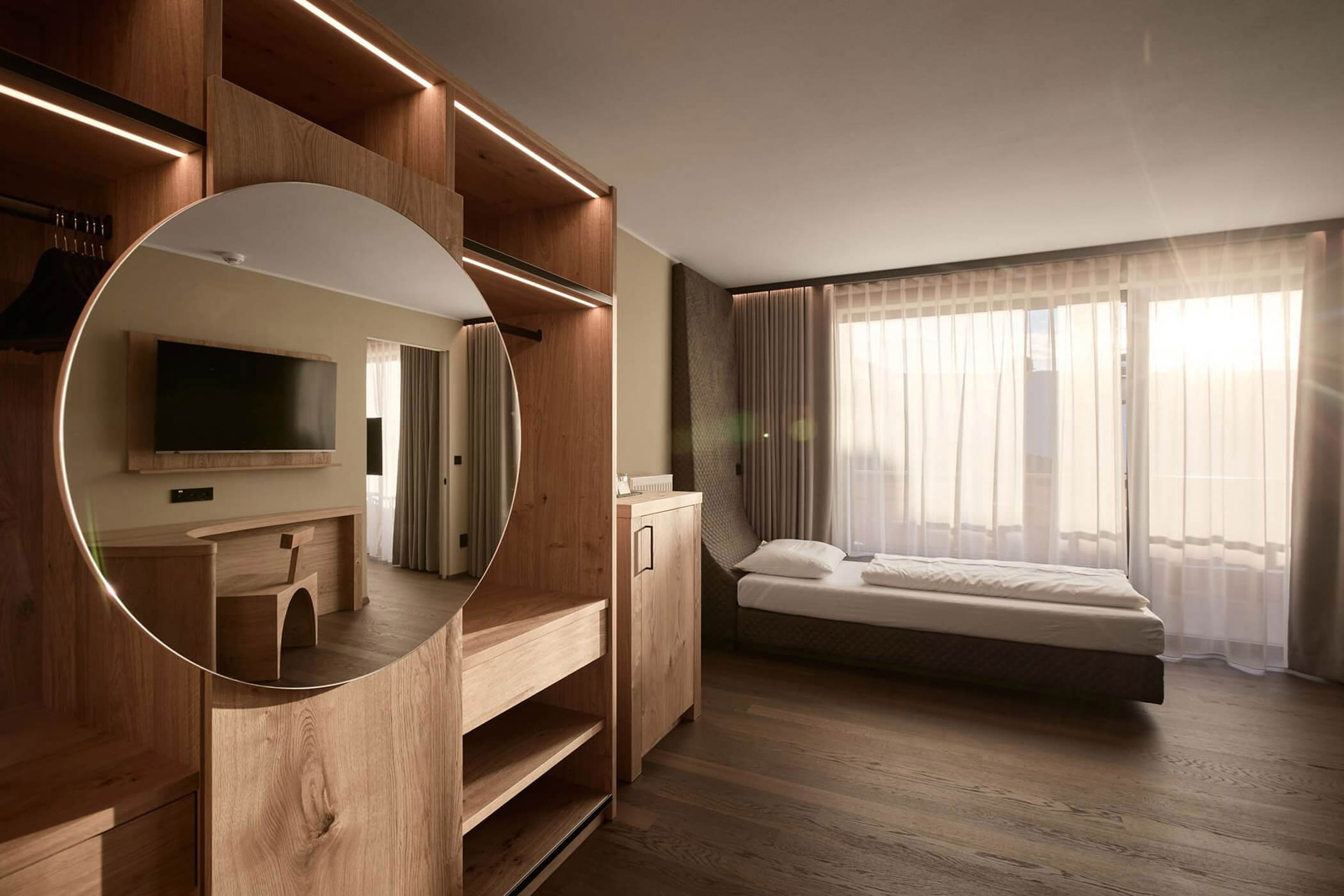 Modernes Hotelzimmer mit einem Holzschrank, an dem ein runder Spiegel angebracht ist, und einem Einzelbett. - Hotel DAS ROYAL