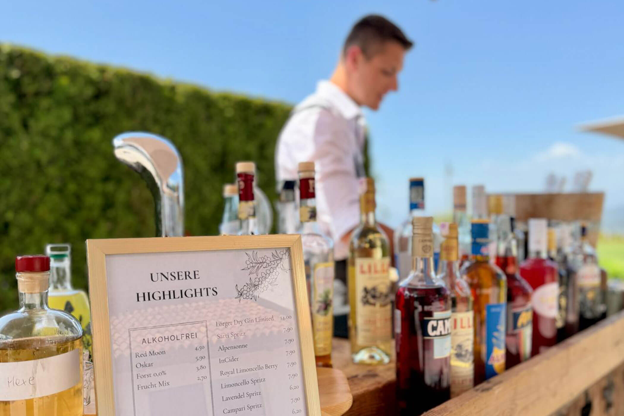 Eine Barkarte mit der Aufschrift Unsere Highlights, die auf einer Theke mit verschiedenen Flaschen ausgestellt ist. - Hotel DAS ROYAL