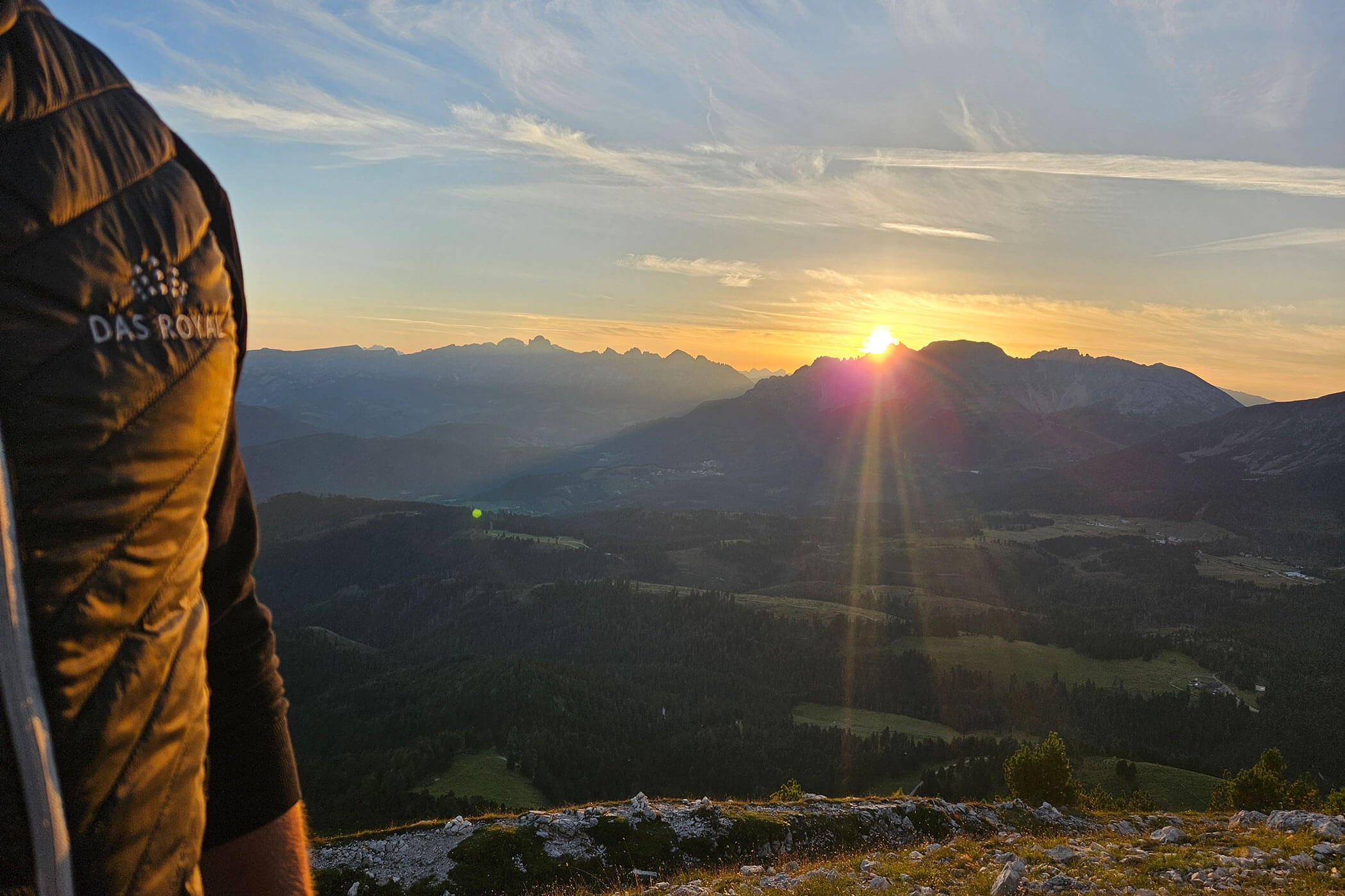 Eine Person, die bei Sonnenuntergang über ein Bergtal blickt. - Hotel DAS ROYAL