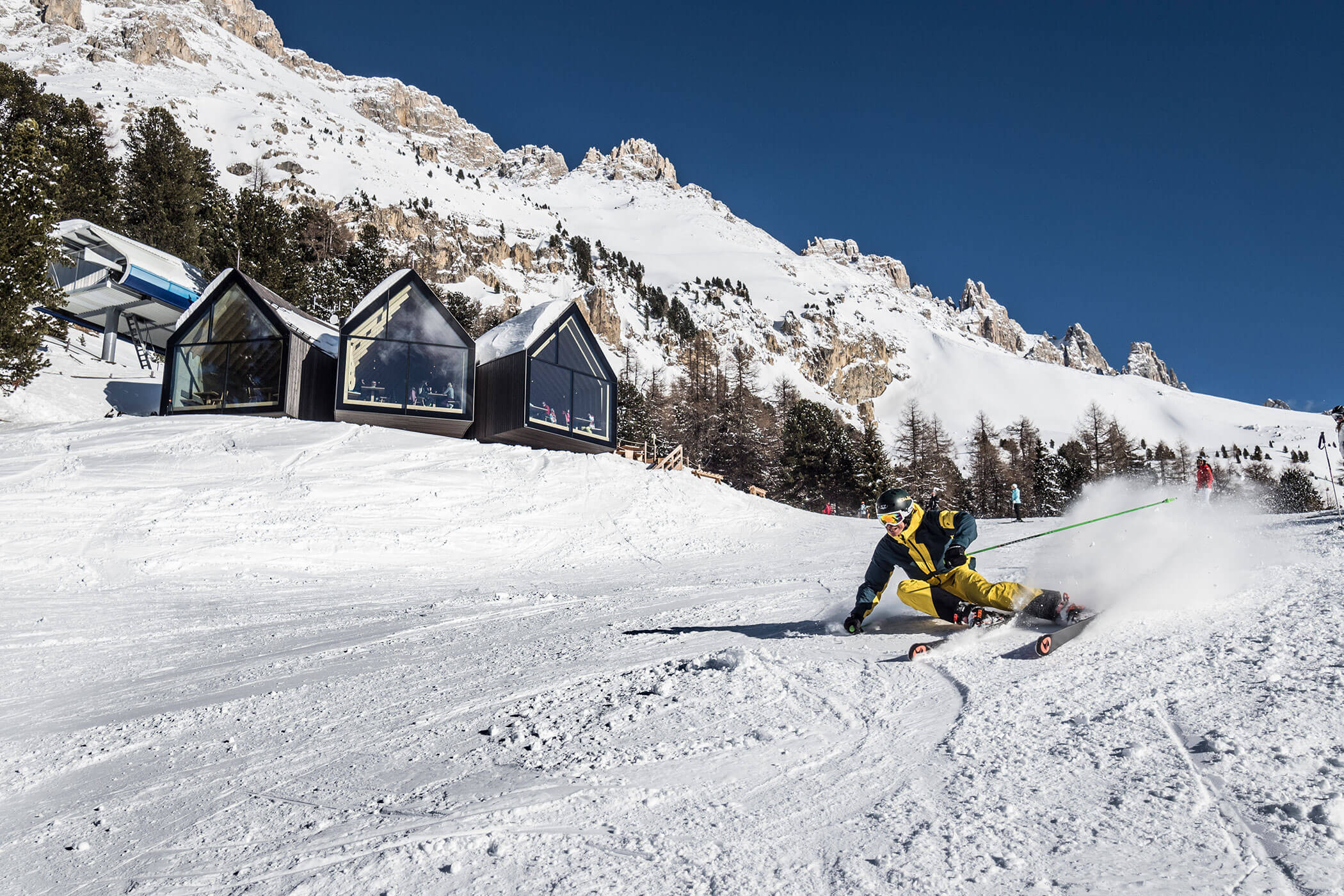 Ein Skifahrer gleitet vor modernen Gebäuden auf einem Berghang durch den Schnee. - Hotel DAS ROYAL