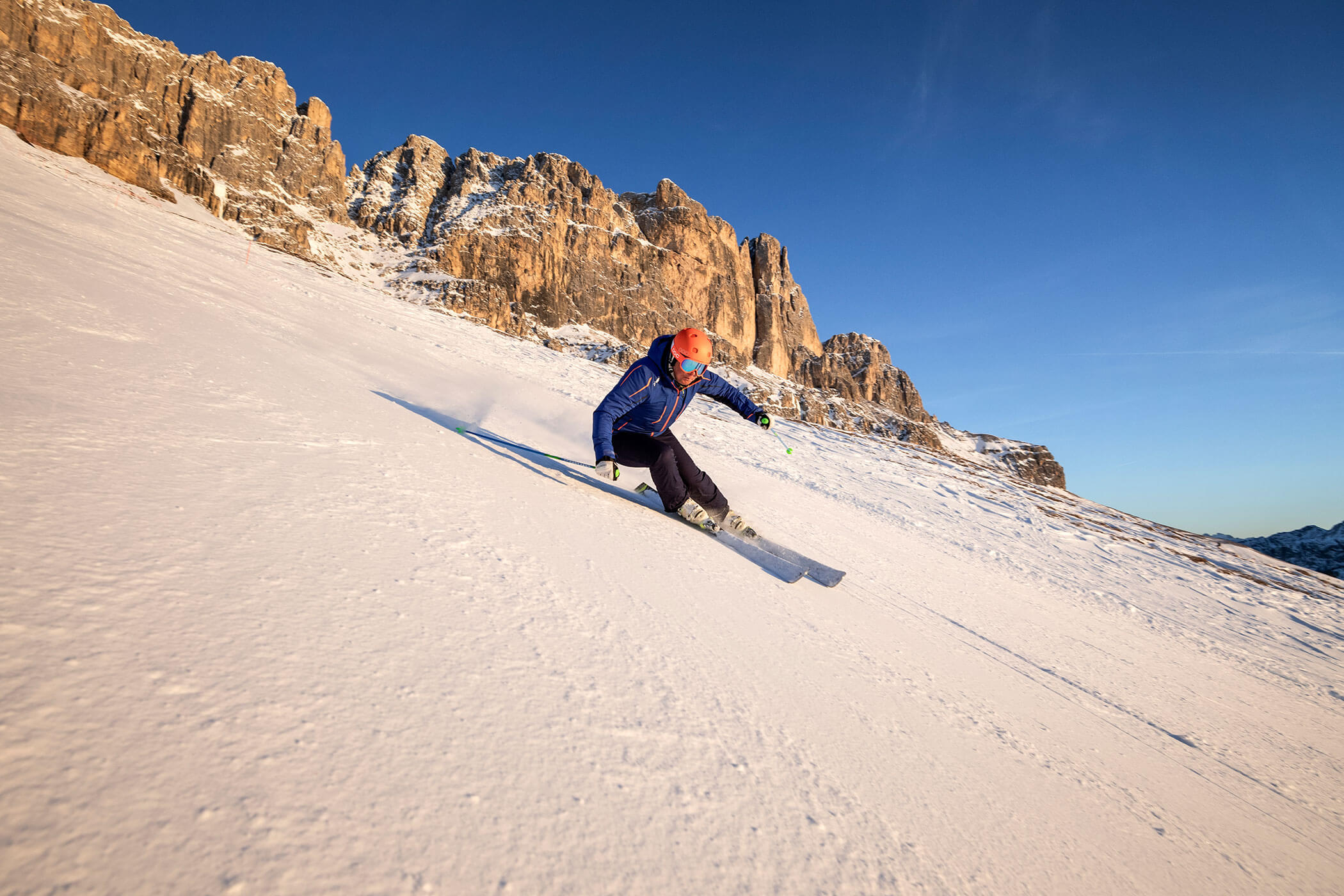 Ein Skifahrer, der unter felsigen Berggipfeln einen verschneiten Hang hinunterfährt. - Hotel DAS ROYAL