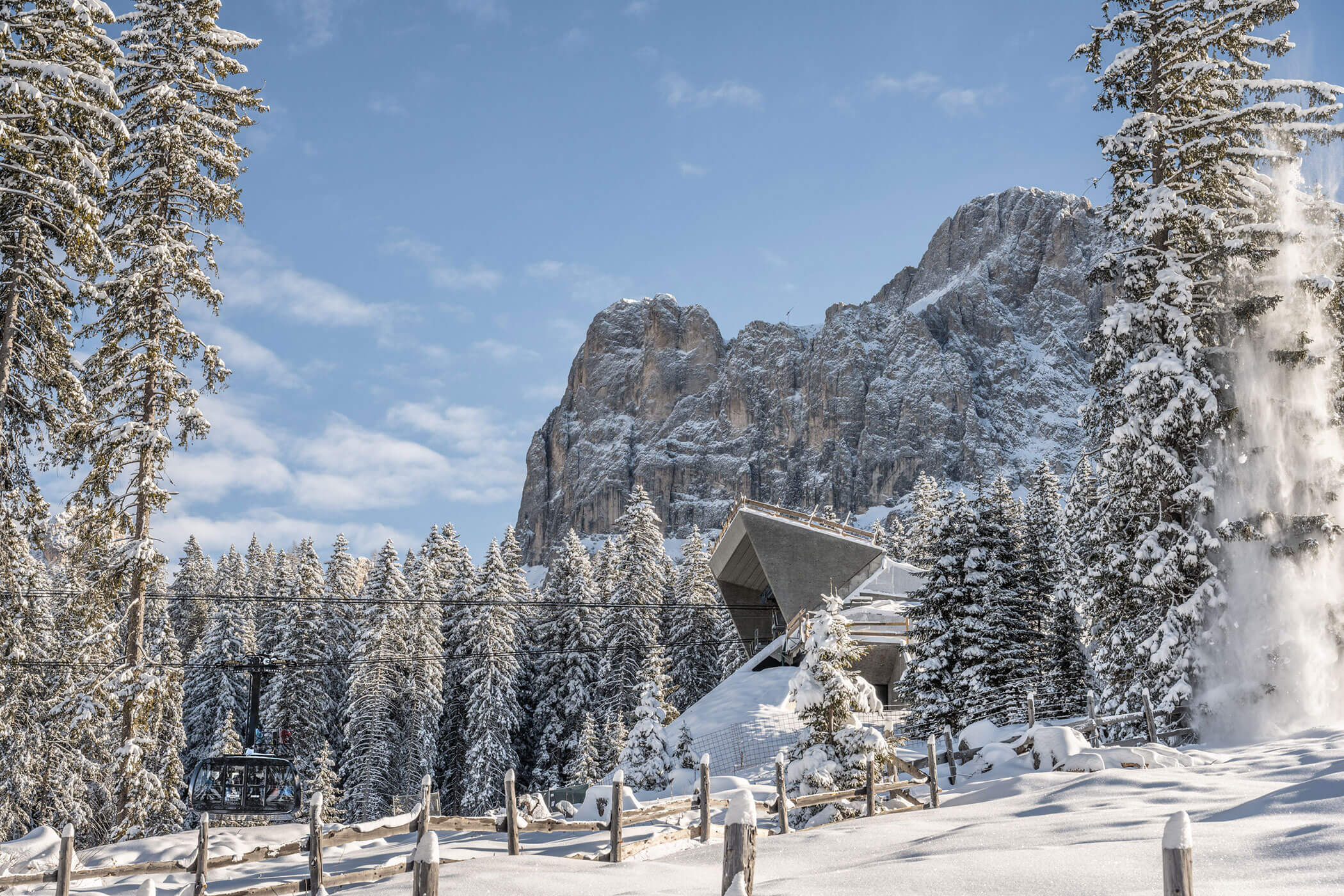 Modernes Gebäude in einem verschneiten Bergwald mit einem Sessellift und felsigen Gipfeln. - Hotel DAS ROYAL