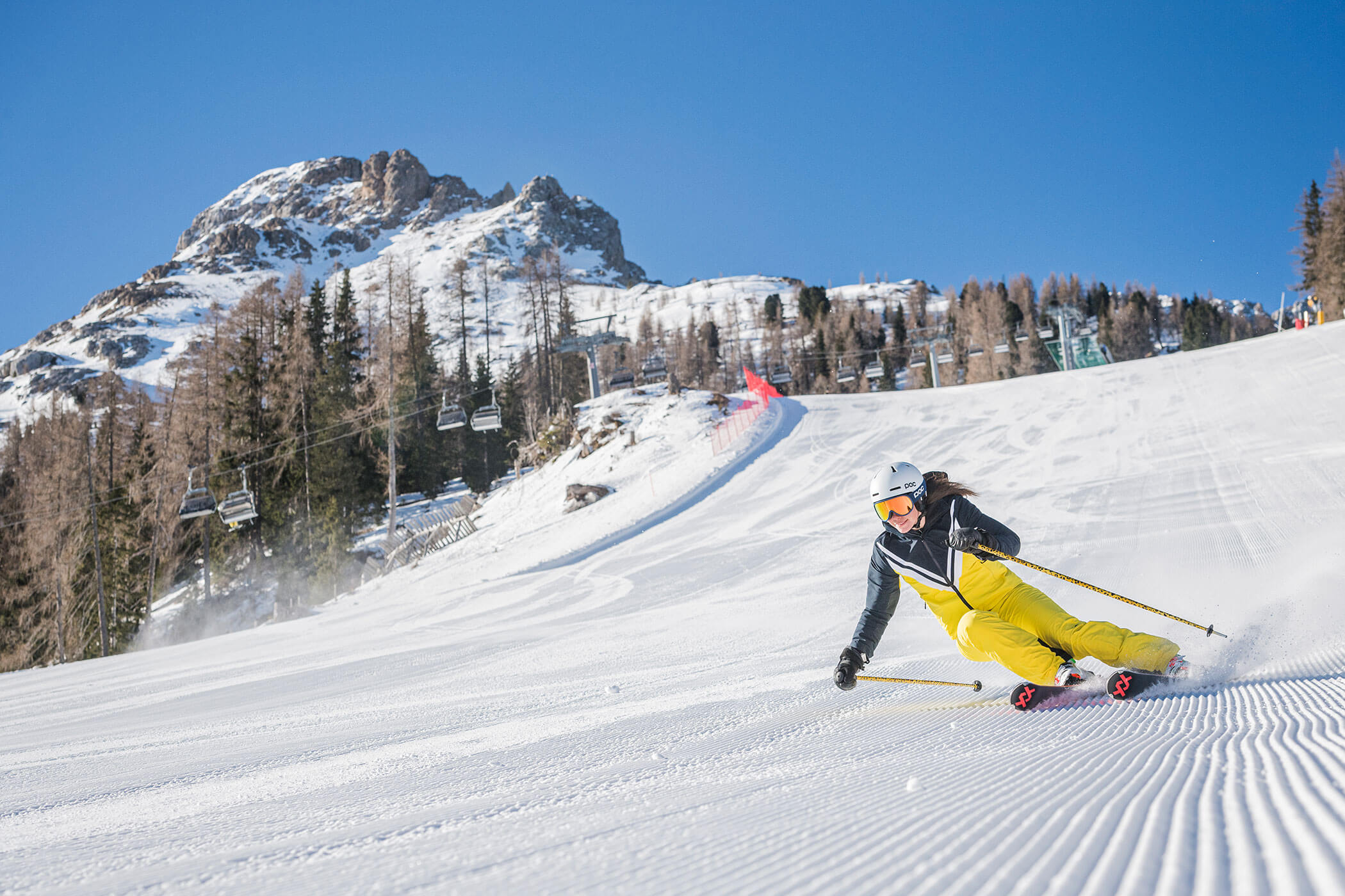 Ein Skifahrer in einem gelben Skianzug saust einen präparierten Hang hinunter. - Hotel DAS ROYAL
