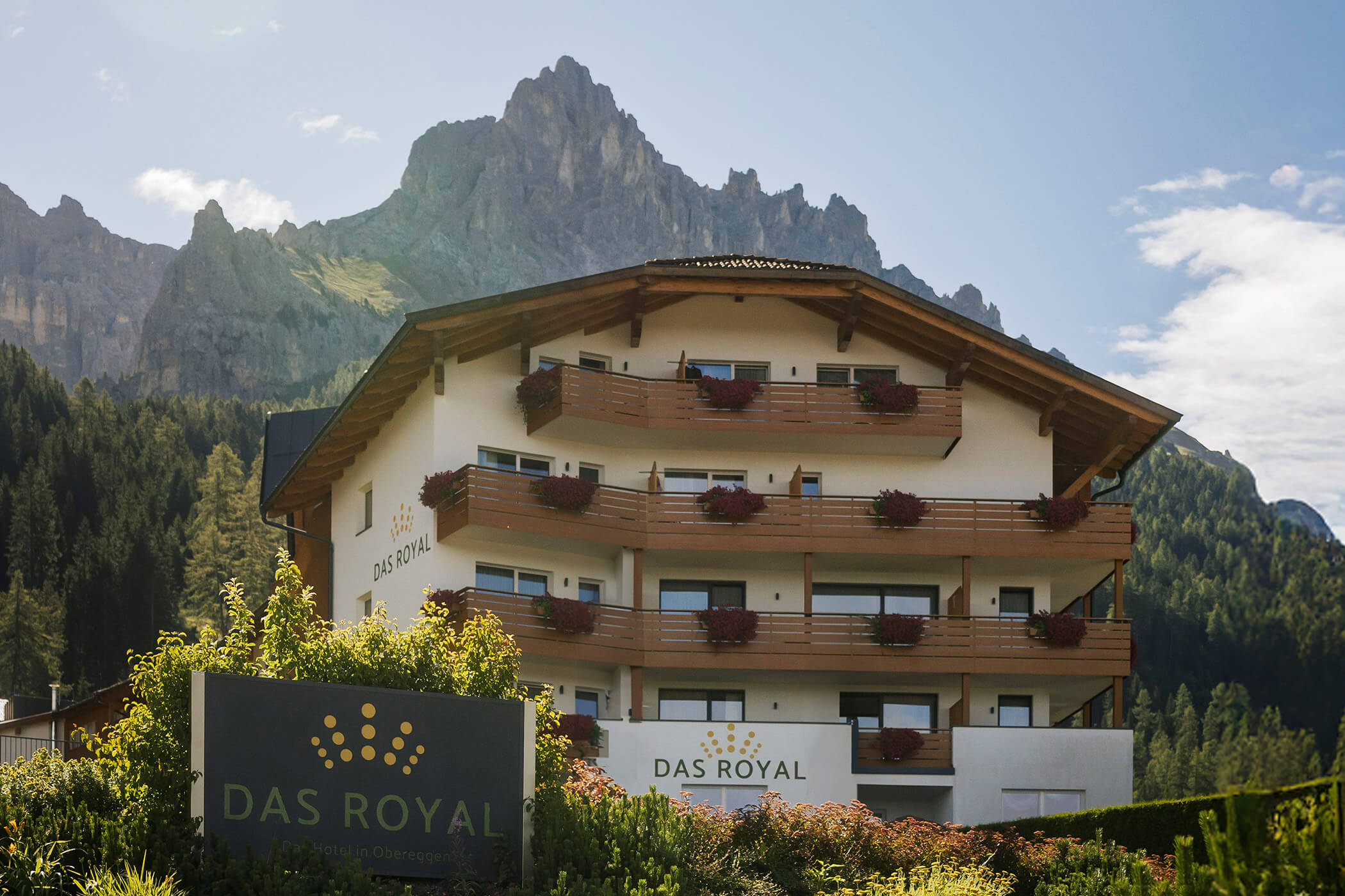 Das Royal Hotel mit Balkonen und Blumenkästen vor einer zerklüfteten Bergkette. - Hotel DAS ROYAL